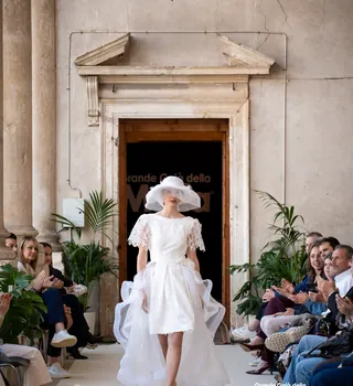 Modella in abito bianco corto con cappello sulla passerella in villa